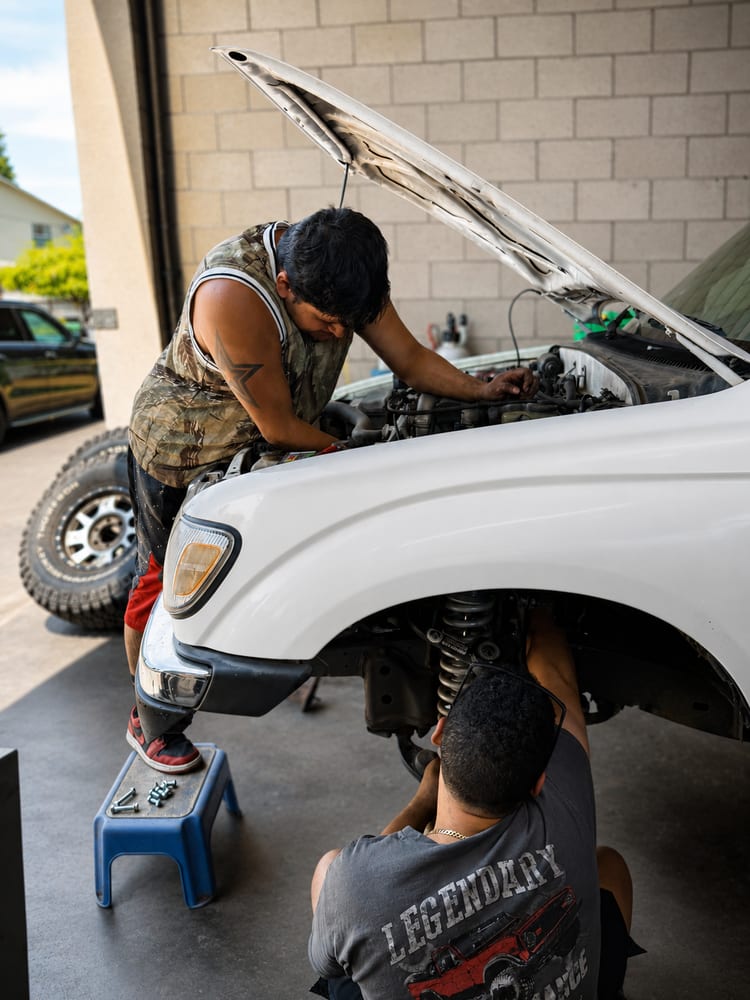 River City Autohaus technicians working on the front suspension of a Toyota truck with the front end apart